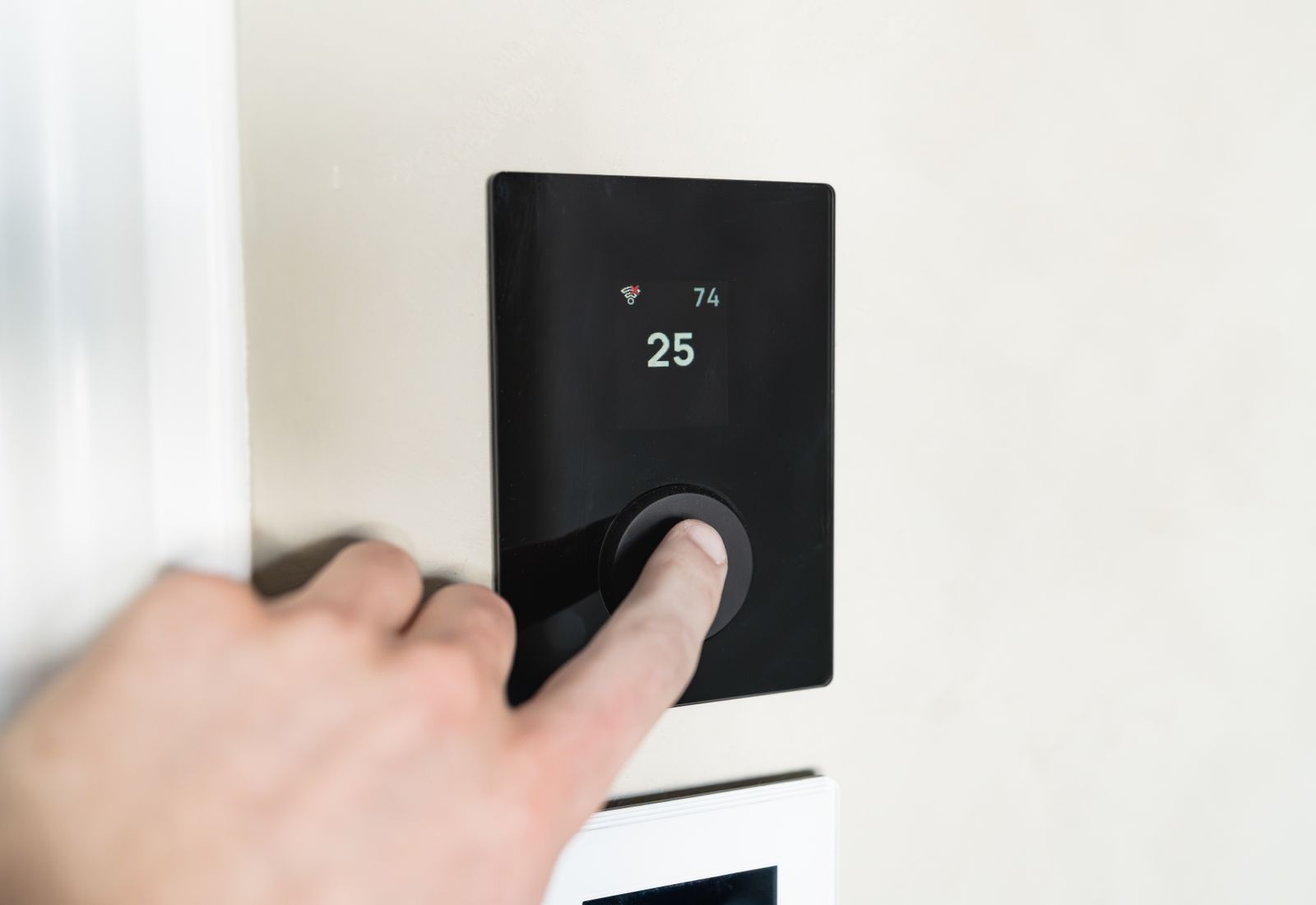 Une main ajustant un thermostat mural moderne